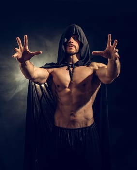 Scary muscular young man with pointed hood and cape on naked body
