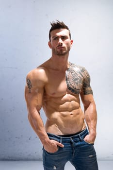 Handsome shirtless athletic man in jeans, with hands in his pockets,, looking away in studio shot, isolated on white background