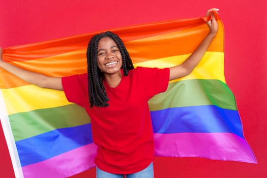 Happy african woman raising a lgbt rainbow flag in studio with red background
