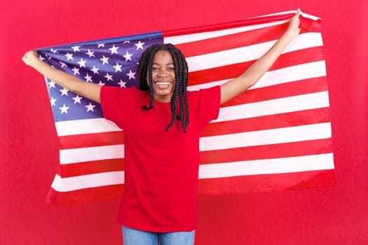 Happy african woman raising a north america national flag in studio with red background