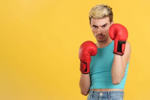 Gay man with boxing gloves in fight pose in studio with yellow background