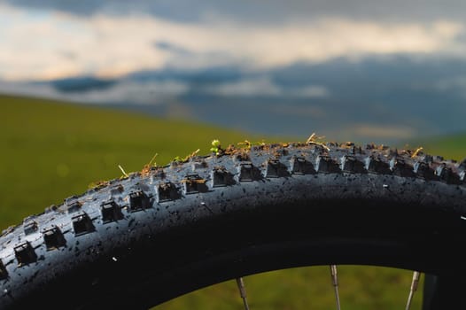 Concept mtb downhill bike theme. Close-up of the tread of an all-terrain mountain bike tire against the backdrop of mountains and sunset sky.