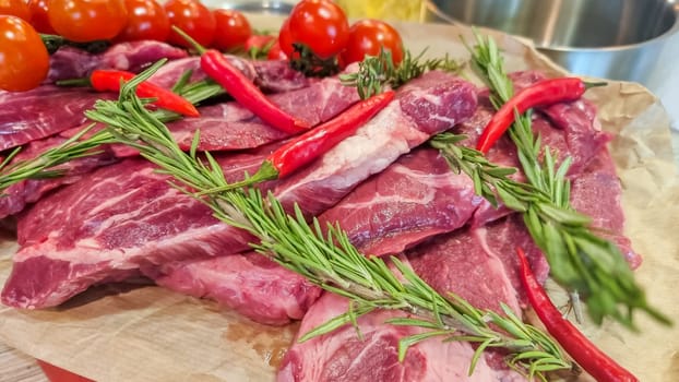 Aluminium foil roll with piece of raw meat, tomatoes, rosemary and spices on color wooden table, closeup