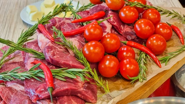 Aluminium foil roll with piece of raw meat, tomatoes, rosemary and spices on color wooden table, closeup