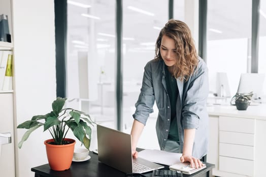 Young Business Woman Embracing Productivity: Using Laptop Computer at Office. Student Girl Thriving in a Modern Workspace. Freelancing, Business Casual, and Dynamic Lifestyle Concept for Success