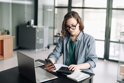 Professional woman accountant managing finances: using calculator and computer in office. Financial planning, budgeting, and accounting concept for business and money management