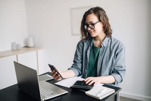 Professional woman accountant working with calculator and laptop computer in office. Smiling businesswoman working remotely from home office. Finance and accounting concept, work-from-home, business