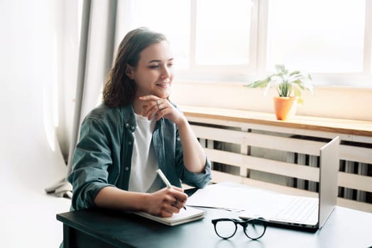 Young woman multitasking with laptop computer at office and student girl working remotely from home. Online work, study, freelance, and modern office lifestyle concept.
