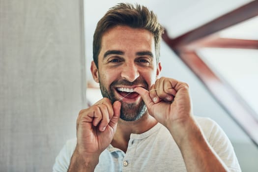 Pay attention to detail. Portrait of a cheerful young man flossing his teeth while looking at his reflection in the mirror at home