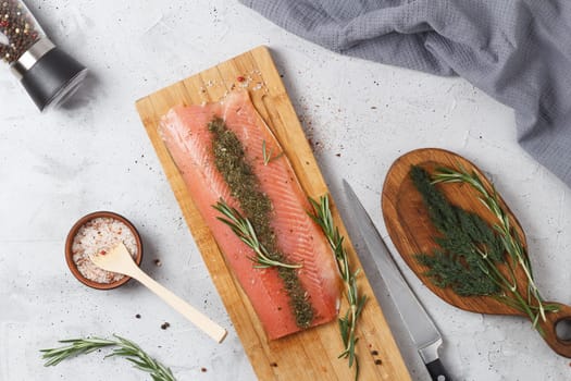 Salted fish fillet with spices and herbs: dill and rosemary on a wooden board on a gray background.