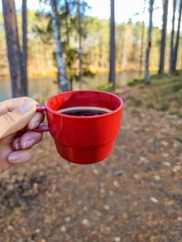 red cup of tea in hand on background autumn leaves