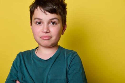 Headshot. Close-up portrait of a Caucasian handsome mischievous teen boy, school kid smiling looking at camera, isolated on yellow background. Children. People. Emotions. Schoolkids. Kids