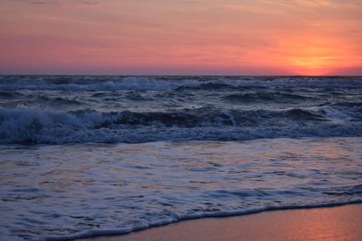 A beautiful sunset on the beach in the turbulent ocean. Shades of orange and blue.