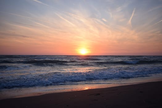 A beautiful sunset on the beach in the turbulent ocean. Shades of orange and blue.