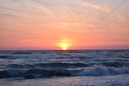 A beautiful sunset on the beach in the turbulent ocean. Shades of orange and blue.