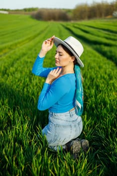 Young attractive woman in white hat, blue shirt, blue jeans, posing in summer green field. Copy, empty space for text