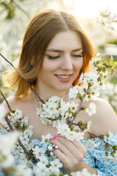 A pretty woman in a blue dress in a blooming spring garden. A gentle woman in a light summer dress.