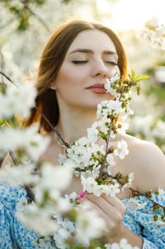 A pretty woman in a blue dress in a blooming spring garden. A gentle woman in a light summer dress.