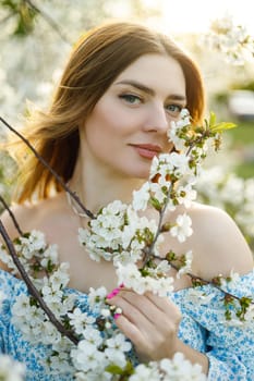 A pretty woman in a blue dress in a blooming spring garden. A gentle woman in a light summer dress.