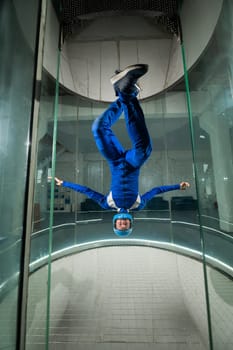 A man in overalls and a protective helmet enjoys flying in a wind tunnel. Free fall simulator.