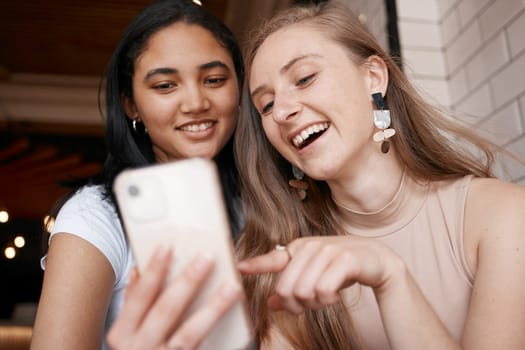 Social media, communication and friends with a comic mobile app on a phone at a cafe. Website, internet and women with a mobile streaming and speaking about a funny video on the web at a coffee shop.