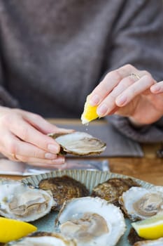 Beautiful Woman eating fresh oysters and drinking in restaurant. Seafood delicacies. oysters with lemon