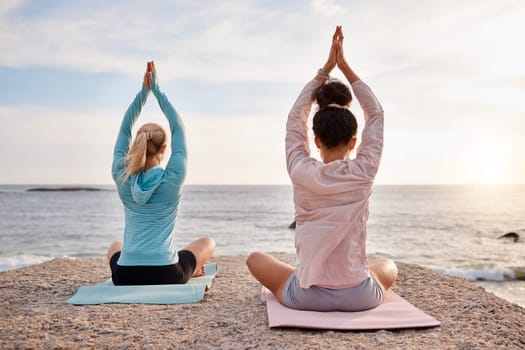 Yoga, back and arms raised on sunrise beach, ocean or sea for morning meditation, chakra balance and bonding. Yogi, women and relax friends on nature rock for zen, healthcare wellness or spirituality.