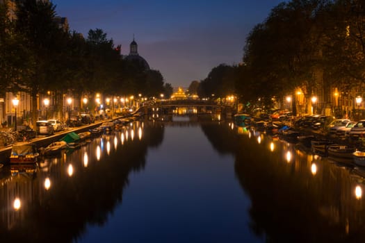 Netherlands. Summer night on the Amsterdam canal. Lanterns and parked cars on the embankments. Boats moored along the banks of the canal