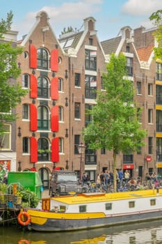 Netherlands. Embankment of the Amsterdam Canal with authentic buildings. Residential barge and bicycles. People queue for fresh pastries in a small bakery