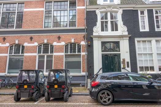 Netherlands. Small cobbled street in Amsterdam. Two mini cars are parked in front of the facade of authentic houses