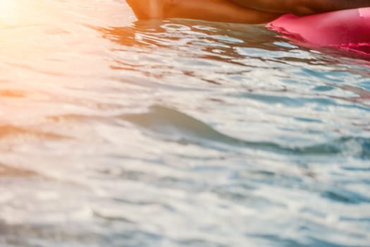 Woman works on laptop in sea. Freelancer, young blond woman in sunglases floating on an inflatable big pink donut with a laptop in the sea at sunset. Freelance, travel and holidays concept