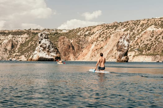 Side view foto of a man swiming and relaxing on the sup board. Sportive man in the sea on the Stand Up Paddle Board SUP. The concept of an active and healthy life in harmony with nature