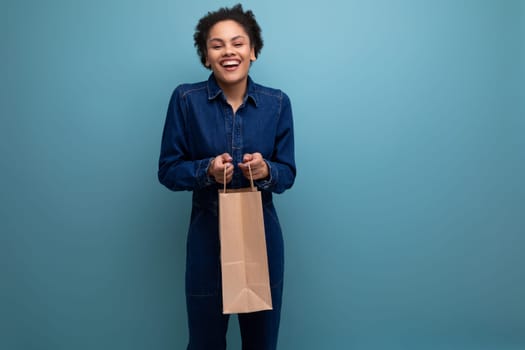 happy positive activist young hispanic brunette woman with fluffy curly hair in blue denim suit holding eco friendly recyclable craft bag.