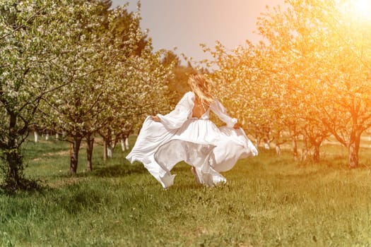 Woman white dress park. A woman in a white dress runs through a blossoming cherry orchard. The long dress flies to the sides, the bride runs rejoicing in life