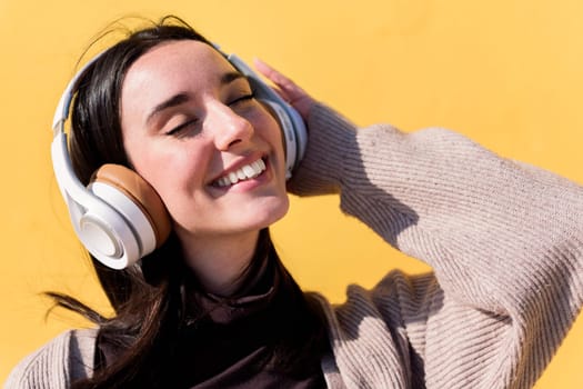 happy young woman listening to music on headphones with yellow background, concept of rhythm and positive people