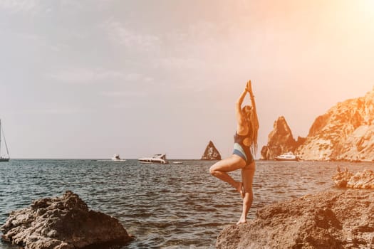 Yoga on the beach. A happy woman meditating in a yoga pose on the beach, surrounded by the ocean and rock mountains, promoting a healthy lifestyle outdoors in nature, and inspiring fitness concept