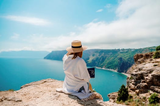 Freelance woman working on a laptop by the sea, typing away on the keyboard while enjoying the beautiful view, highlighting the idea of remote work