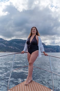 Woman on a yacht. Happy model in a swimsuit posing on a yacht against a blue sky with clouds and mountains.