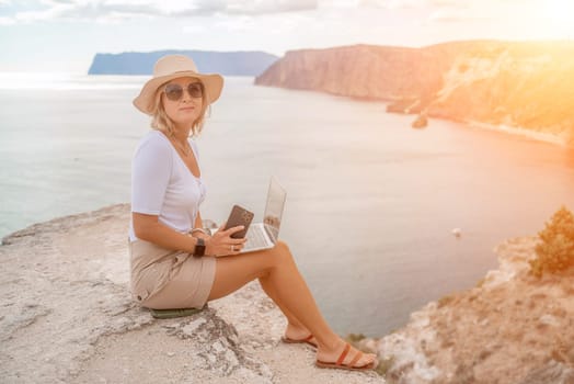 Freelance women sea working on the computer. Good looking middle aged woman typing on a laptop keyboard outdoors with a beautiful sea view. The concept of remote work