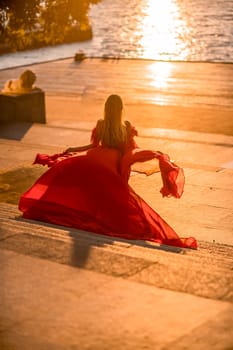 Sunrise red dress. A woman in a long red dress against the backdrop of sunrise, bright golden light of the sun's rays. The concept of femininity, harmony