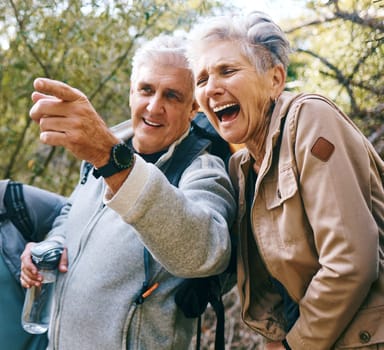 Senior hiking couple, funny and outdoor adventure by trees, woods or forest for health in summer. Elderly man, pointing and woman with comic joke, laugh and bonding together for wellness in sunshine.