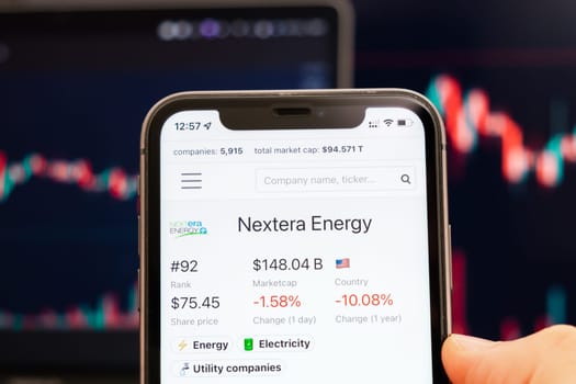 Nextera Energy stock price on the screen of cell phone in mans hand with changing stock market exchange with trading candlestick graph analysis, February 2022, San Francisco, USA