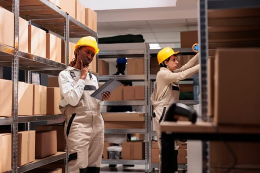 African american woman logistics operator thinking about inventory in warehouse, holding digital tablet and rubbing chin. Storehouse supervisor managing parcels transportation