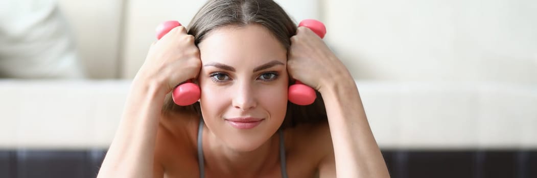 Beautiful smiling woman lies and holds dumbbells closeup. Home fitness and workout concept