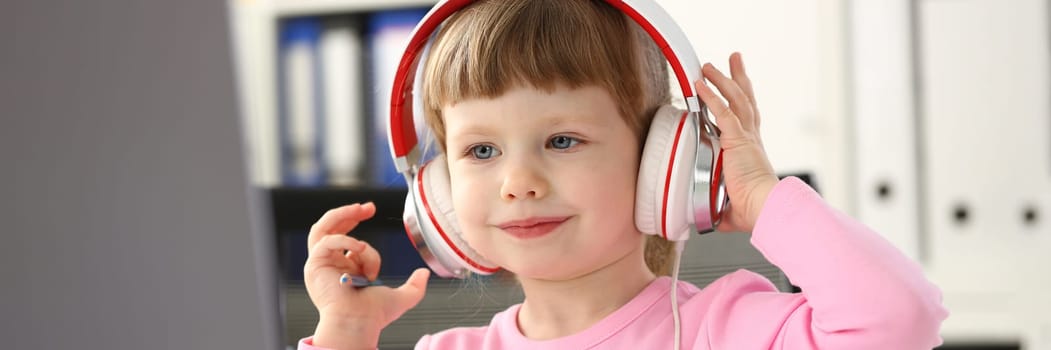 Portrait of cute girl in headphones watching cartoons using laptop computer. Distance learning and home education for children