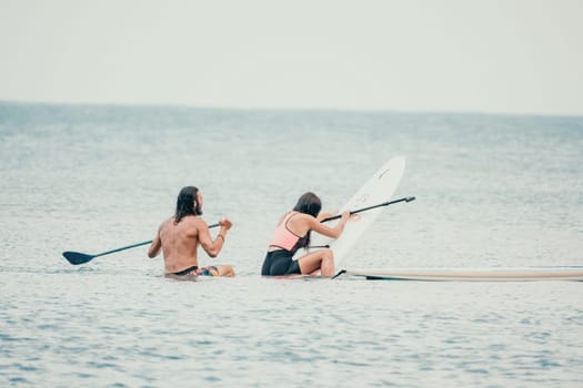 Sea woman and man on sup. Silhouette of happy young woman and man, surfing on SUP board, confident paddling through water surface. Idyllic sunset. Active lifestyle at sea or river