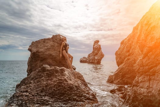 Woman swimsuit sea. Attractive blonde woman in a black swimsuit enjoying the sea air on the seashore around the rocks. Travel and vacation concept