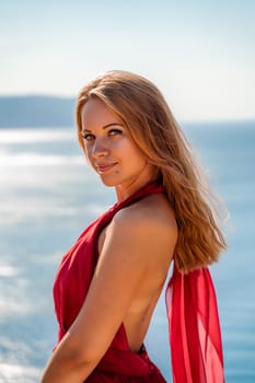 Smiling young woman in a red dress looks at the camera. A beautiful tanned girl enjoys her summer holidays at the sea. Portrait of a stylish carefree woman laughing at the ocean