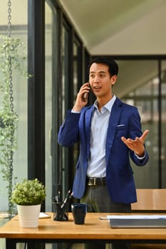 Portrait of successful financier investor answering or giving consultation to customer on mobile phone near office window.