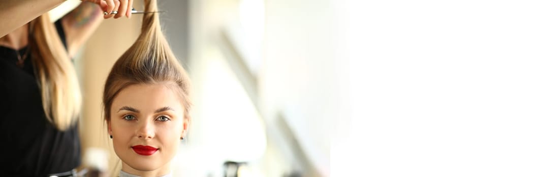 Portrait of blonde woman in hairdressing salon with long ponytail. Master hairdresser cuts hair concept